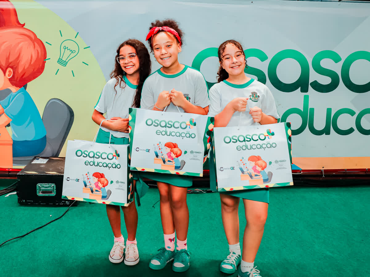 Três alunas de uniforme com as sacolas do programa, no dia da entrega dos kits