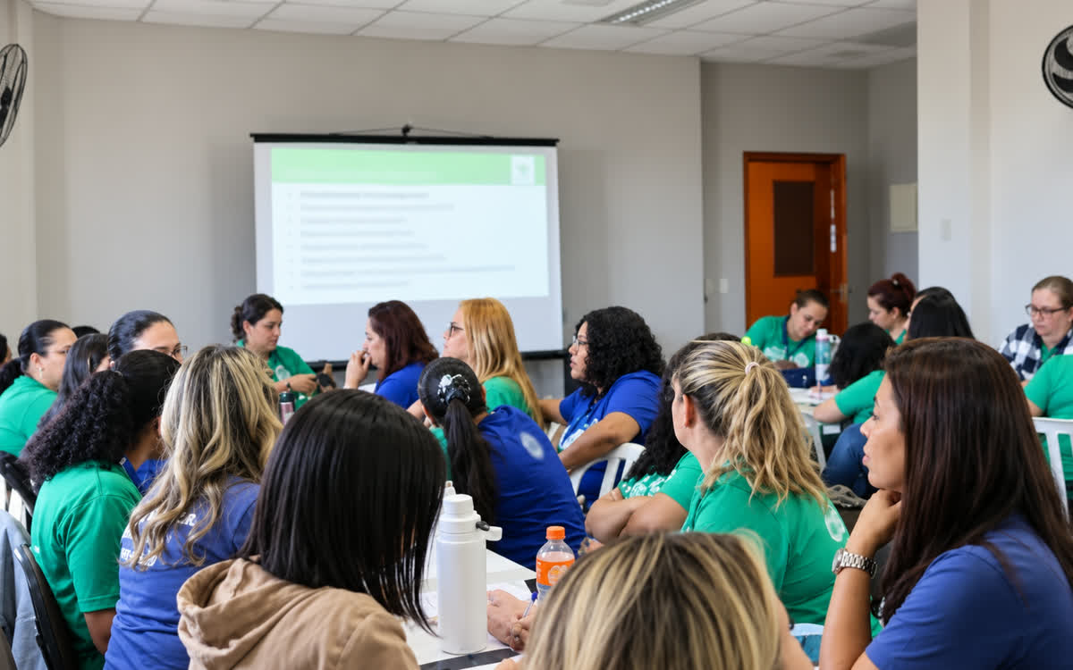 Professoras da rede municipal em formação, acompanhando uma apresentação projetada