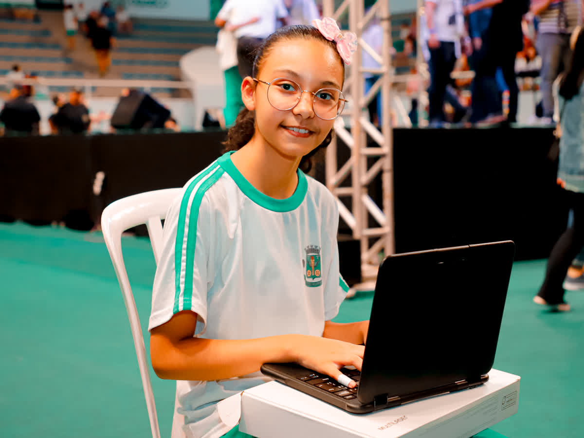 Aluna de uniforme usa o notebook do kit, apoiado sobre a própria caixa